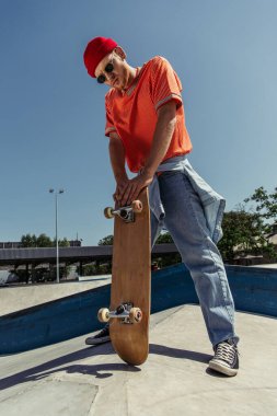 full length of trendy skater standing with skateboard outdoors