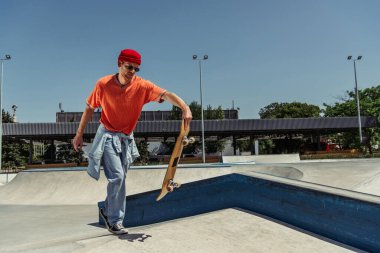 stylish skater in jeans and sunglasses carrying skate on ramp