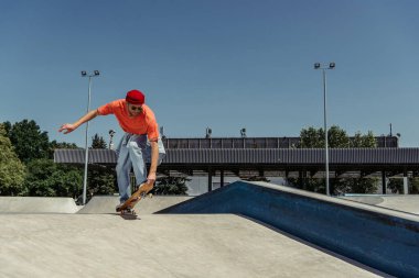 young man in stylish clothes skateboarding on ramp in park