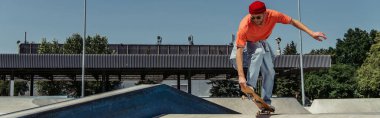 trendy man in sunglasses jumping with skateboard while training in park, banner