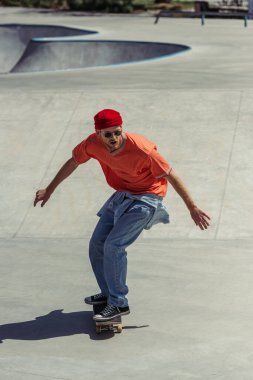 young man in beanie and jeans skateboarding on ramp in park