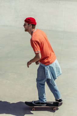 side view of man in orange t-shirt and red beanie riding skateboard