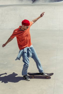 full length of stylish man with outstretched hands skateboarding in skate park