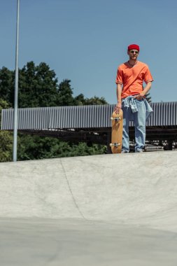 full length of trendy man in sunglasses standing with hand in pocket in skate park
