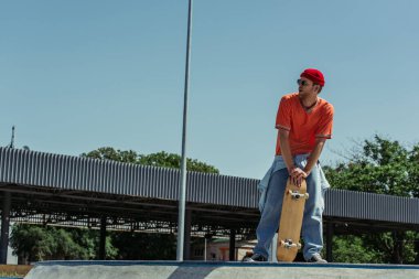 full length of fashionable man with skateboard looking away outdoors