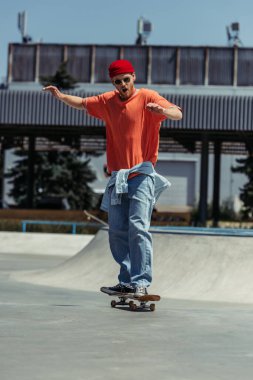 full length of excited man in trendy outfit riding skate on ramp
