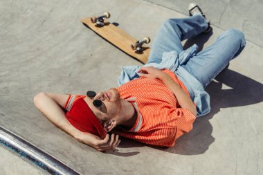 high angle view of trendy man in sunglasses relaxing on ramp near skateboard