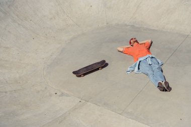 high angle view of trendy man lying near skateboard in skate park