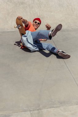 cheerful man in sunglasses falling down from skateboard