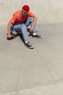 young man in gumshoes sitting on skateboard in skate park