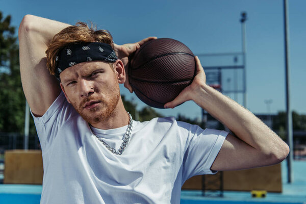 redhead man in bandana and necklace holding ball and looking at camera