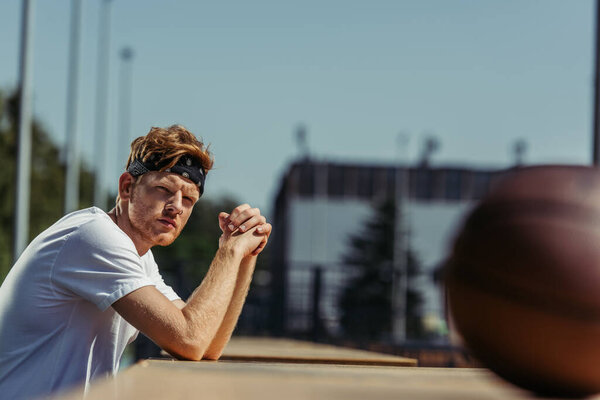 sportive man in white t-shirt and headband near ball on blurred foreground