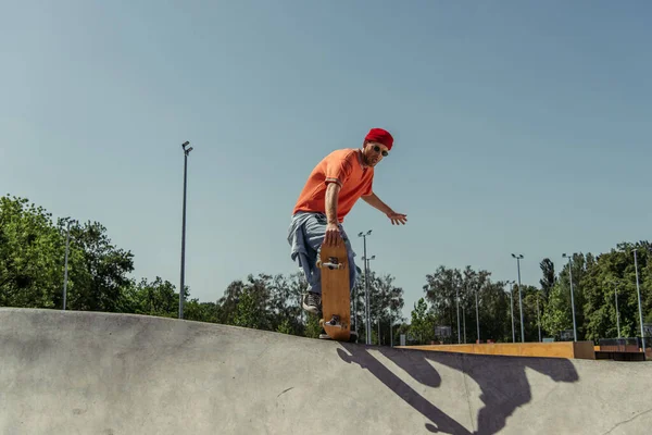 young skateboarder in sunglasses jumping from ramp in skate park