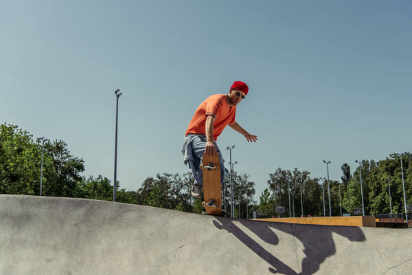 молодой скейтбордист в солнцезащитных очках прыгает с трамплина в скейт-парке