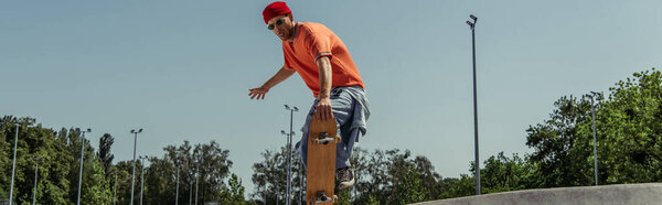 модный молодой человек в солнечных очках катается на скейтборде в парке, баннер
