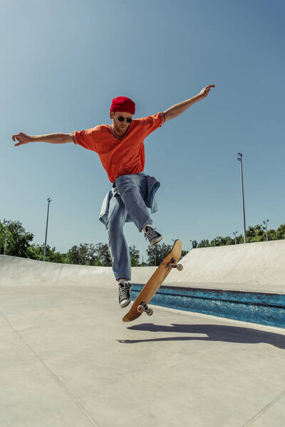 молодой человек с протянутыми руками прыгает на скейтборде в скейт-парке