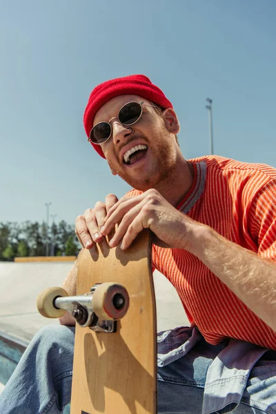 excited man in sunglasses laughing near skate outdoors