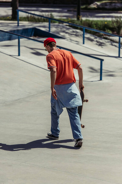Вид сзади человека в красном, то есть идущего со скейтбордом в скейт-парке