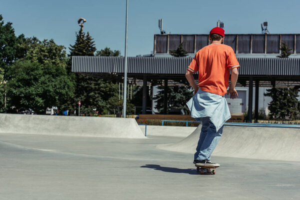 назад вид человека в оранжевой футболке скейтбординг в городском скейт-парке