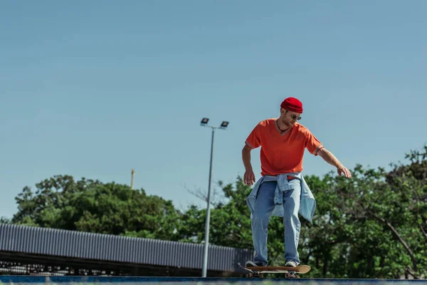 full length of fashionable man skateboarding under blue sky