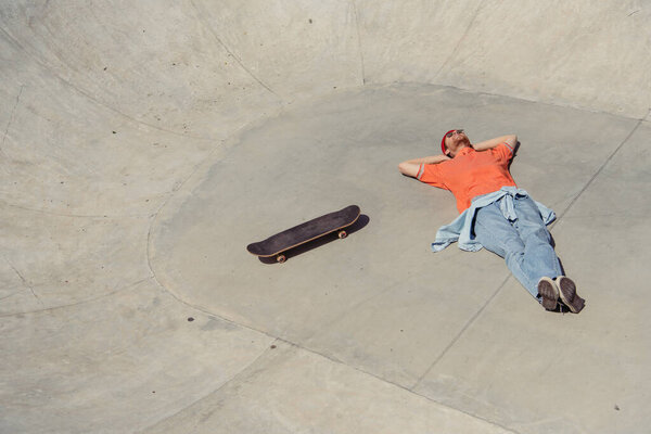 высокий угол обзора лежащего рядом с скейтбордом человека в скейт-парке