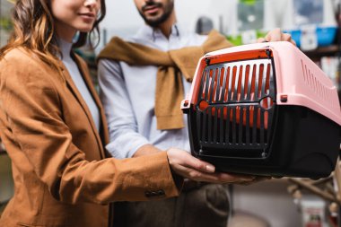 Cropped view of woman holding animal cage near blurred boyfriend in pet shop 