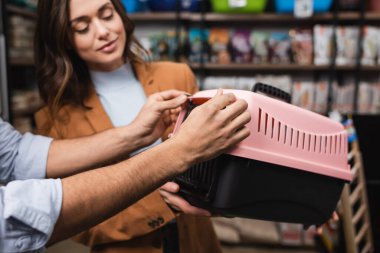 Man holding animal cage near blurred girlfriend in pet shop