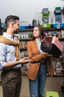 Smiling woman holding animal cage near muslim boyfriend in pet shop 