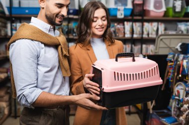 Smiling muslim man looking at animal cage near girlfriend in pet shop 