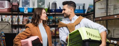 Positive interracial couple holding animal cages in pet shop, banner 