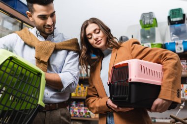 Low angle view on smiling multiethnic couple holding animal cages in pet shop