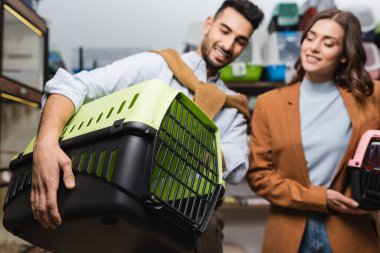 Blurred interracial couple holding animal cages in pet shop 