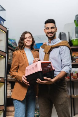 Positive interracial couple holding animal cage in pet shop 