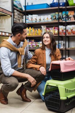 Positive interracial couple talking near animal cages in pet shop 