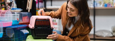 Brunette woman looking at animal cage in pet shop, banner 