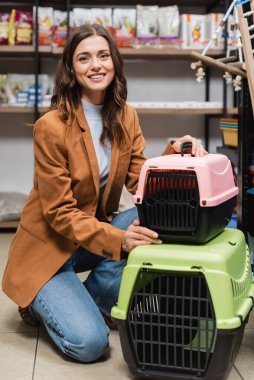 Smiling woman looking at camera near animal cages in pet shop 