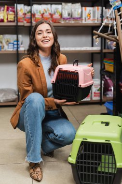 Cheerful woman holding animal cage and looking at camera in pet shop 