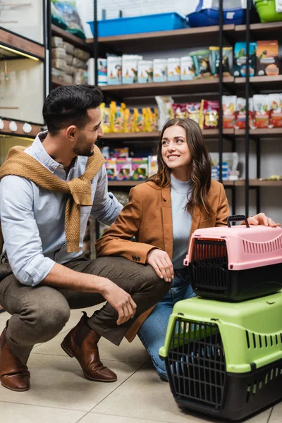 Positive interracial couple talking near animal cages in pet shop