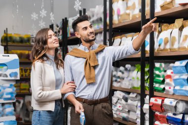 Smiling muslim man pointing at showcase near girlfriend in pet shop