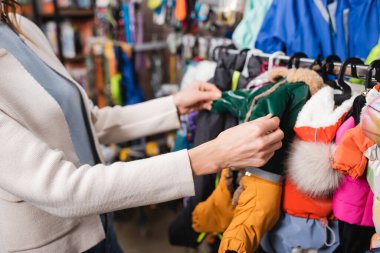 Cropped view of woman choosing animal jackets in blurred pet shop  clipart