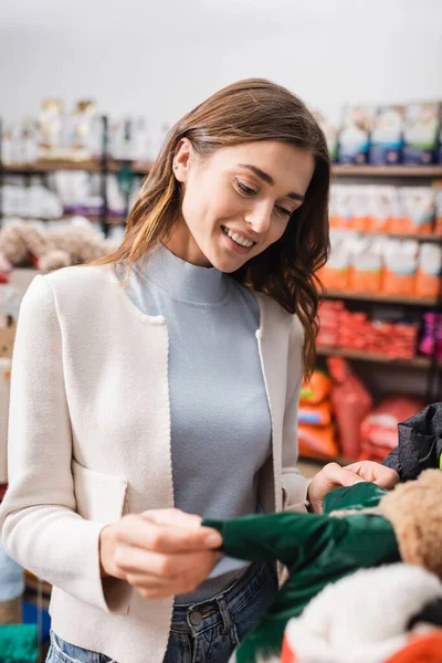 Smiling woman choosing animal clothes in pet shop