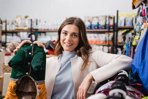 Счастливая женщина держит одежду животных и смотрит в камеру в зоомагазине 