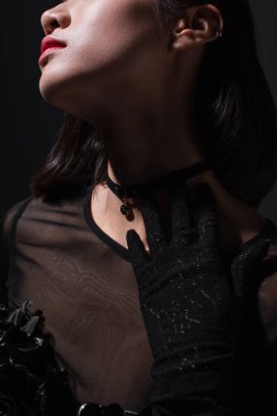cropped view of brunette young woman in black glove touching neck isolated on black