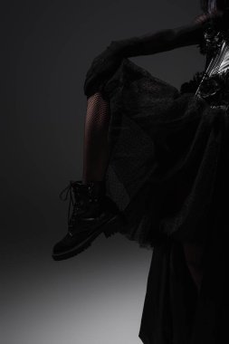 cropped view of woman in gothic dress and black boot posing on grey