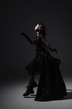 side view of asian young woman in black gothic dress and gloves levitating on dark grey