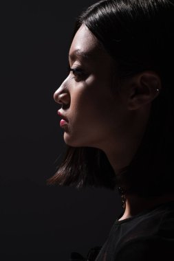 side view of pretty and young asian woman looking away isolated on black