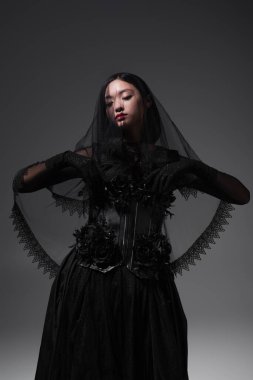 young asian model in gothic outfit with black veil posing isolated on grey