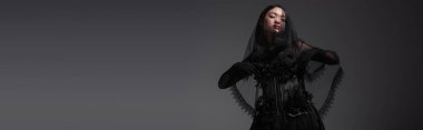 young asian model in gothic outfit with black veil posing isolated on grey, banner
