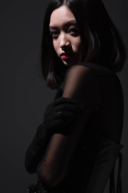 portrait of sensual asian woman in gothic black outfit looking at camera isolated on grey clipart
