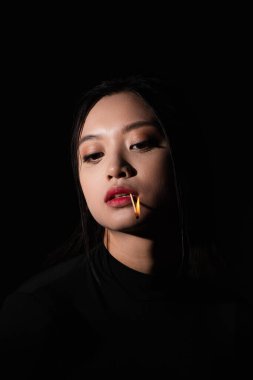 portrait of pretty asian woman with burning matchstick in mouth isolated on black